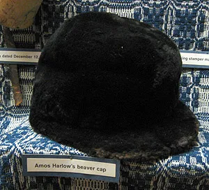 A dark fur cap with a short brim resting on a patterned blue-and-white textile.