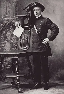 A man in a plumed hat and uniform posing next to a brass horn and sheet music on a small table.