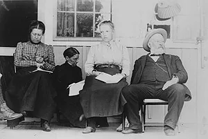 Three women holding papers and an elderly bearded man in a hat sit in a row.