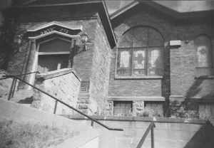 A stone building with steps leading to an entrance with Hebrew script and arched stained glass.